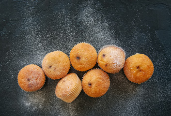 Set of vanilla muffins with chocolate cream filling sprinkled with powdered sugar. Black stone background.