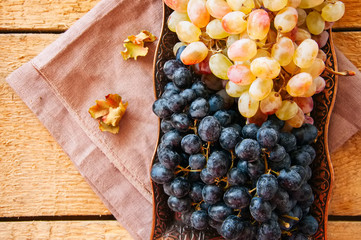 Bunches of fresh ripe grapes served on a vintage tray on a wooden background. Close up and top view.