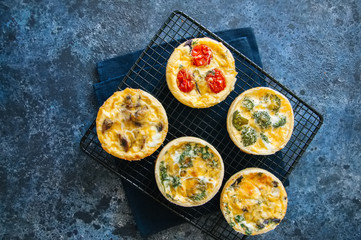 Set of savory mini tarts. Vegetable quiches with tomatoes, mushrooms, herbs, broccoli. Blue stone...