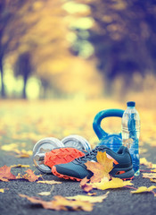 Pair of blue sport shoes water and  dumbbells laid on a path in a tree autumn alley with maple...
