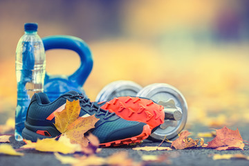 Pair of blue sport shoes water and  dumbbells laid on a path in a tree autumn alley with maple leaves -  accessories for run exercise or workout activity