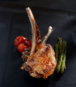 grilled lamb steak with asparagus and tomatoes on a black background