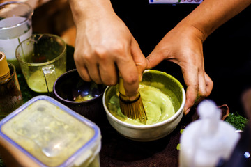 Close up of woman's hands Use a brush maker. Tea powder and water, stir to combine  placed on wooden desktop