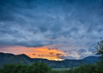 Beautiful dramatic sunset in the mountains. Landscape with sun light shining through orange clouds