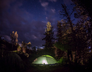 Glowing tent in the mountains under a starry sky