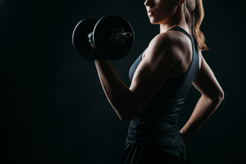girl exercising squatting with dumbbell on black background with copy space