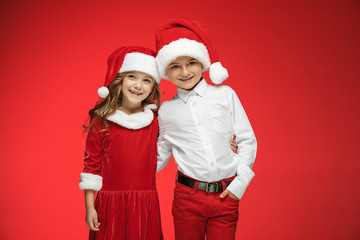 Two happy boy and girl in santa claus hats with gift boxes at studio