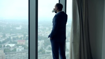 Young businessman drinking coffee and admire view from window in office