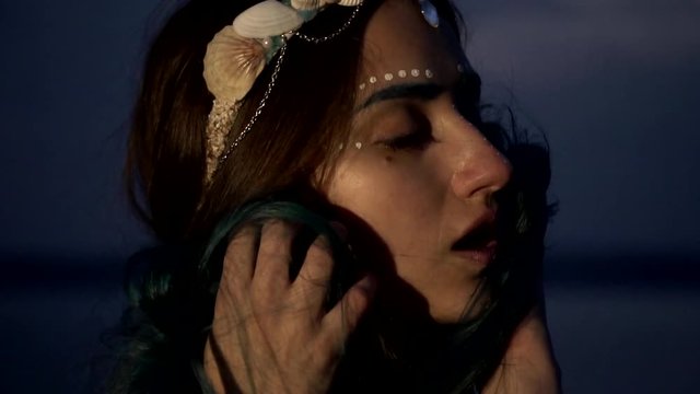 A girl with a beautiful make-up pushes her hair to her face on her head with a cliquish crown of seashells