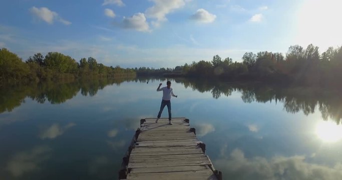 Giovane ragazzo sta ballando allegramente su un molo di legno di un lago
