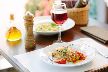 Italian food - delicious lasagne in white plate on table with red wine.