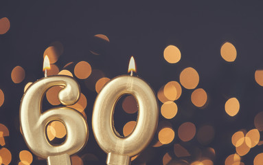Gold number 60 celebration candle against blurred light background