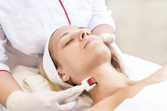 The woman undergoes the procedure of medical micro needle therapy with a modern medical instrument derma roller. 