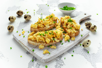 Homemade Quail Scrambled eggs on crispy toast, bread with green onion, chives on white board.