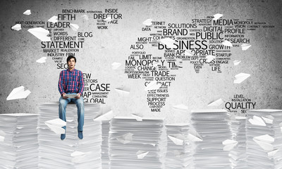 Attractive man sitting on pile of paper documents.