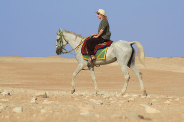 Urlauberin mit Strohhut und khaki Kleidung auf Pferd in der Wüste
