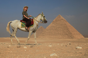 Frau steht alleine mit ihrem Pferd vor den Pyramiden in Ägypten