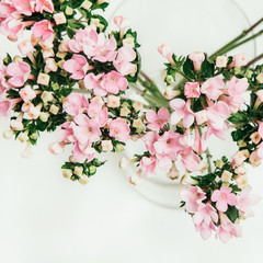 Blossom background of rosy bunch of flowers in glass vase on white backdrop, top view. Spring holidays, Mother's and Women's day gift and decoration concept