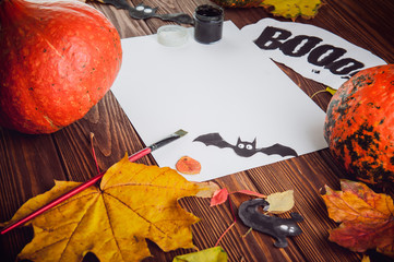 Halloween holiday background. Prepearing for party. Fresh pumpkins, coloured leaves, art, craft and painting materials on dark wooden table. Selective focus, top view. Space for text