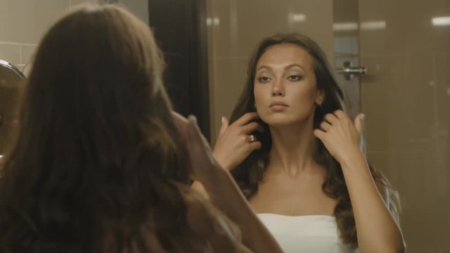 Well-groomed girl corrects her hair in front of the mirror