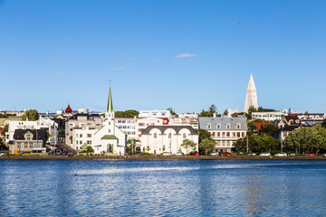 Obraz premium Reykjavik cityscape, with the bell tower of the Hallgrimskirkja church, viewed from across the Tjornin lake in the heart of Iceland capital city on a sunny summer day.