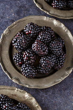 top view on blackberries in plate on dark table background.