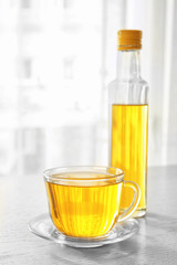 Glass cup and bottle with oil on light wooden table