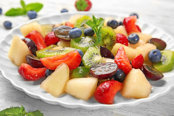 Plate with delicious fruit salad on table