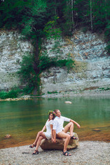 Young couple hugging and kissing on stone near the mountain river. A man and a woman stand against the background of the rocks. Nature. summer. full length. looking at each other.