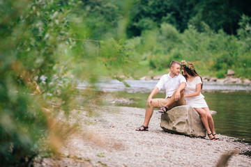 Young couple hugging and kissing on stone near the mountain river. A man and a woman stand against the background of the rocks. Nature. summer. full length. looking at each other.