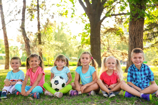 Cute little children with ball sitting on green grass in park