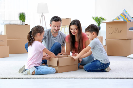 Happy family unpacking moving boxes in room at new home