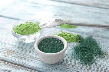 Spirulina and barley grass powder in bowls on wooden background