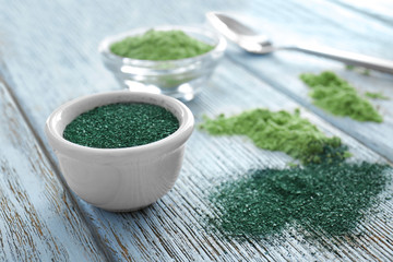 Spirulina powder in ceramic bowl on wooden background