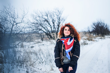 Fototapeta na wymiar a young girl walks in the field. Dressed in winter clothes, she has blue eyes and thick red hair . Hair curls , the color of fire .