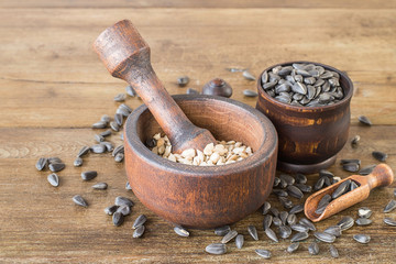  Old round mortar with a pestle with peeled sunflower seeds, next to a small wooden cup with...