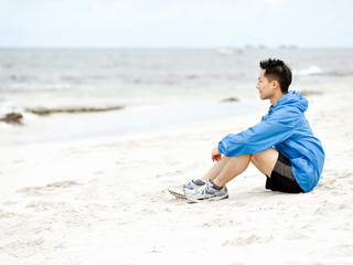 Young man sitting at the beach in sportswear