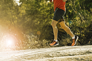 sport man with ripped athletic and muscular legs running downhill off road in jogging training...