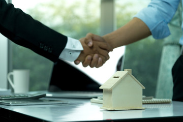 Estate agent sitting in a desk shaking hands with customers after signing a home purchase contract.