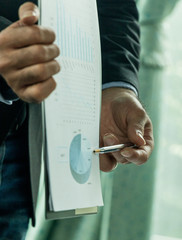 A side view of a businessman analyzing a series of graphs with colleagues while meeting summaries of sales and holding a map with statistics in hand.