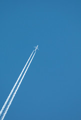 Airplane flying at high altitude leaving its white wake over blue sky