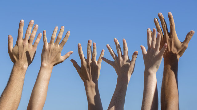 Group raising hands against blue sky background