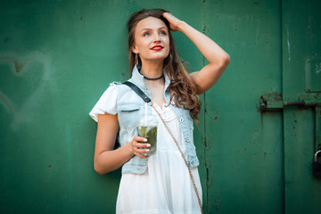 Beautiful woman standing near green garage door background, with cup drink fresh