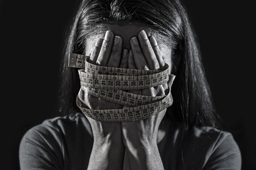hands wrapped in tailor measure tape covering face of young depressed and worried girl suffering anorexia or bulimia nutrition disorder - obrazy, fototapety, plakaty