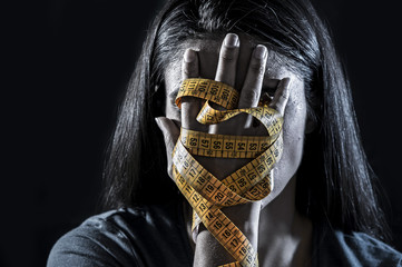 hands wrapped in tailor measure tape covering face of young depressed and worried girl suffering anorexia or bulimia nutrition disorder - obrazy, fototapety, plakaty