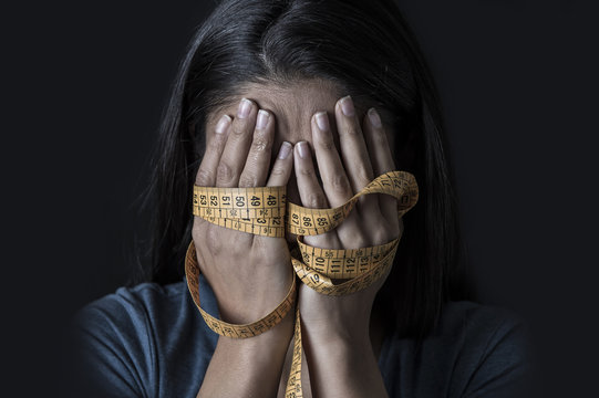 hands wrapped in tailor measure tape covering face of young depressed and worried girl suffering anorexia or bulimia nutrition disorder