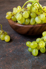 Branch of a green grapes on a wooden plate on a dark background with copy space and selective focus