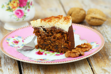 Slice of delicious carrot cake with walnuts with marzipan icing on pink plate
