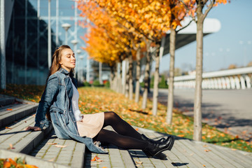 Pretty young woman sitting and relaxing on a stairs in autumn city background.