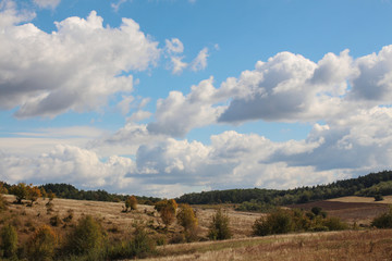 Landscape with beautiful fluffy clouds over autumn field